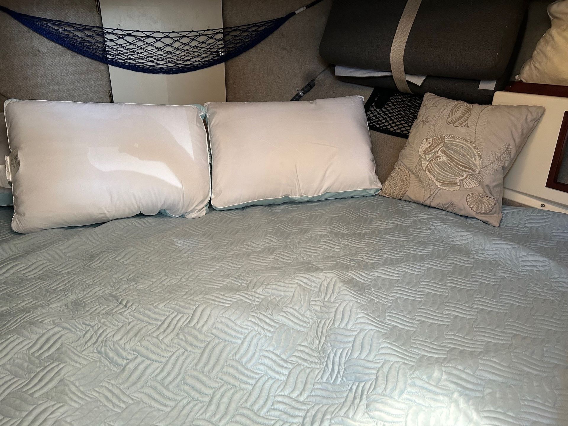 Bed with light blue textured blanket and pillows. Two white square pillows and a tan patterned pillow.