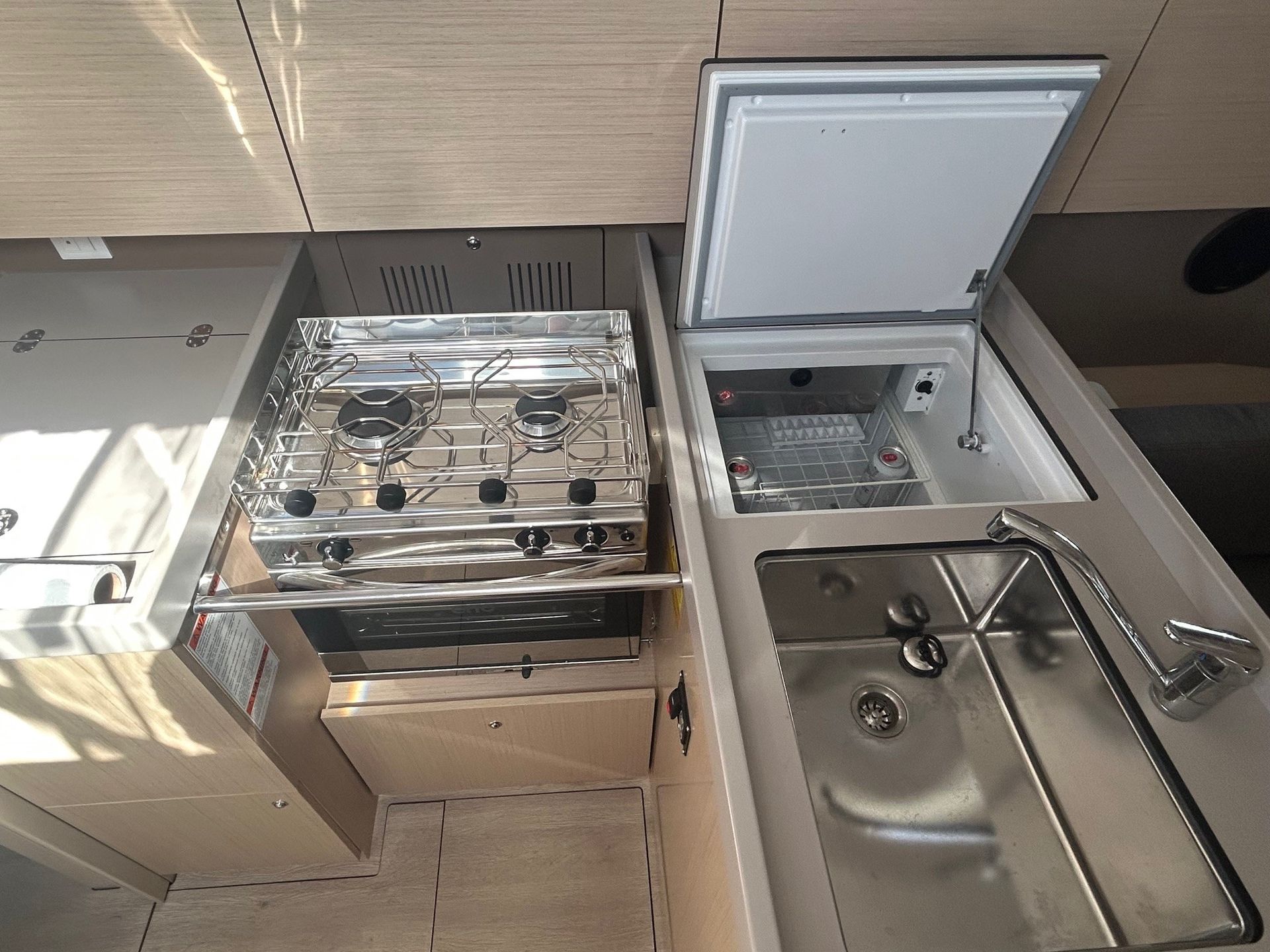 Kitchen area with a stove, refrigerator, and sink inside a vehicle or boat.