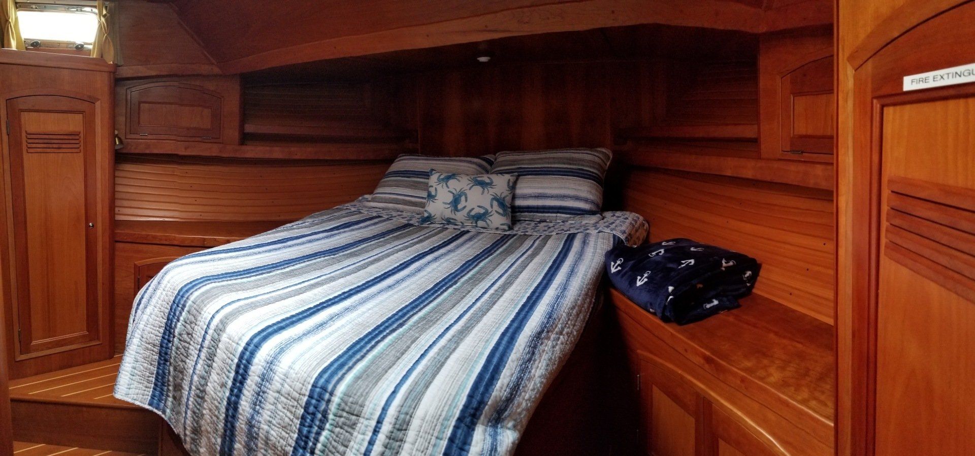 A bed with a blue and white striped blanket is in a wooden cabin on a boat.