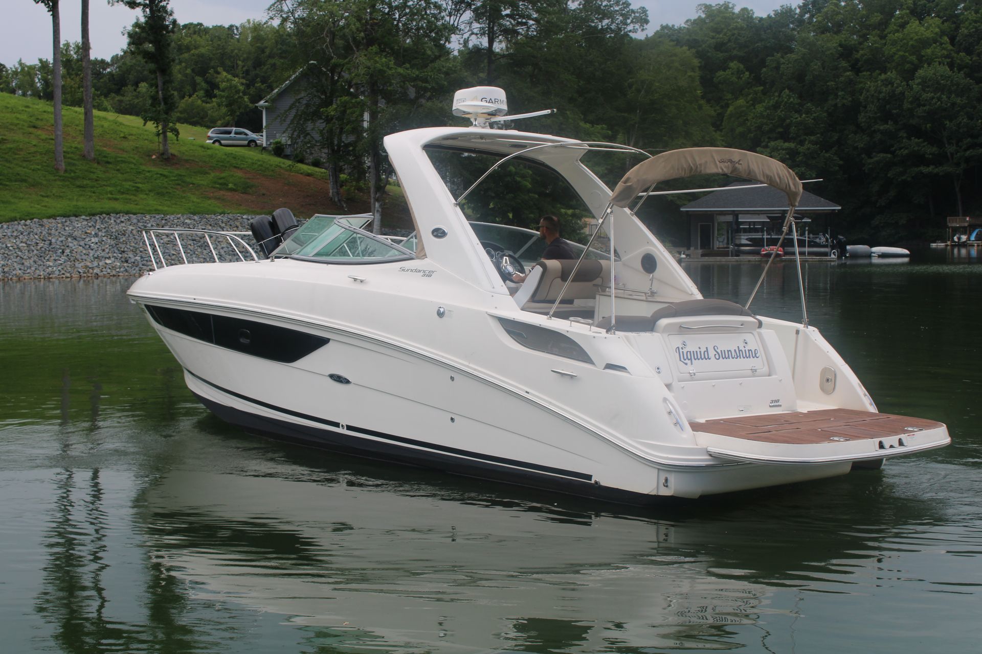 White motorboat on calm water, in a lake or river. Trees and a shoreline are in the background.