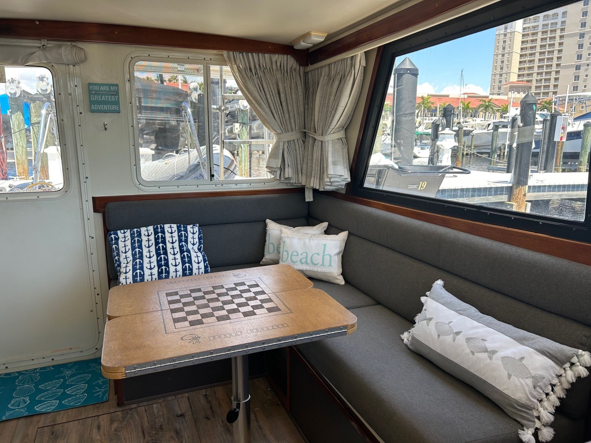 Boat cabin interior with seating, chess table, window view of a marina.