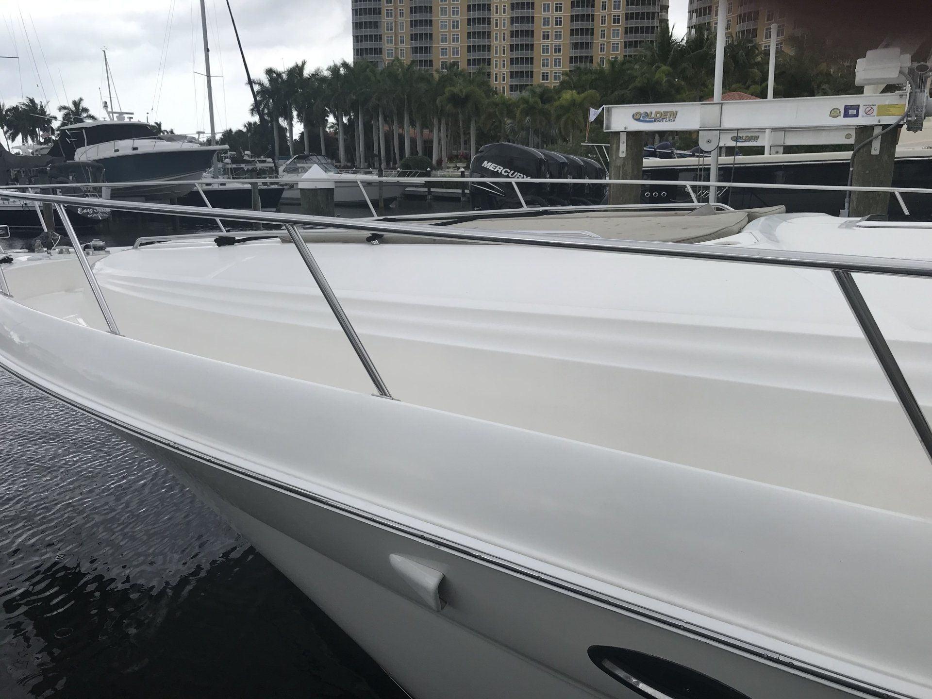 A white boat is docked in a marina with a building in the background.