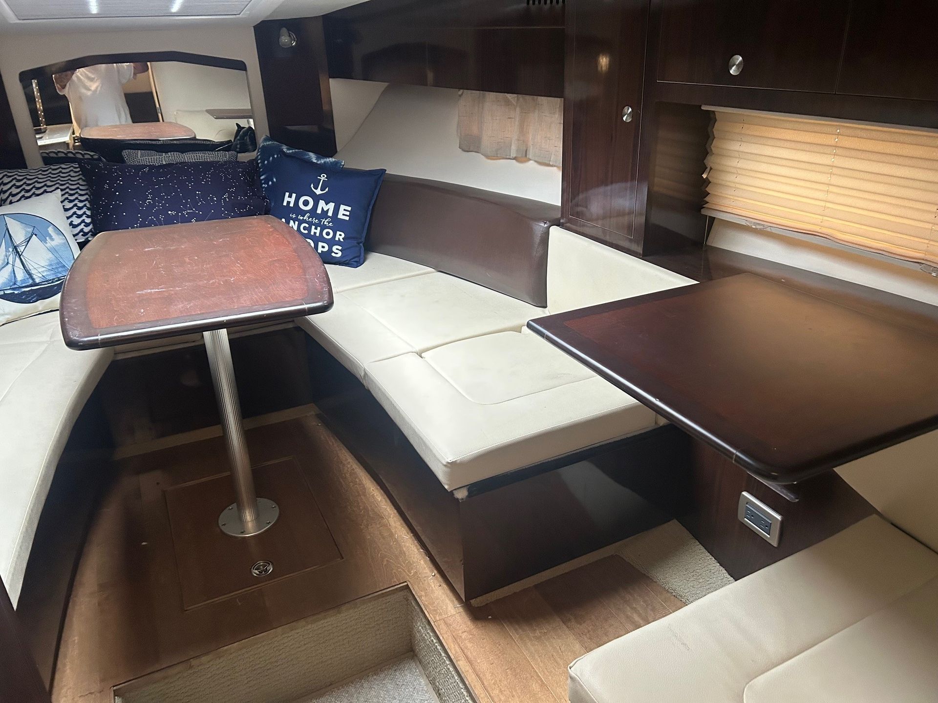 Interior of a yacht cabin with seating, tables, and pillows. Brown and beige tones dominate the space.