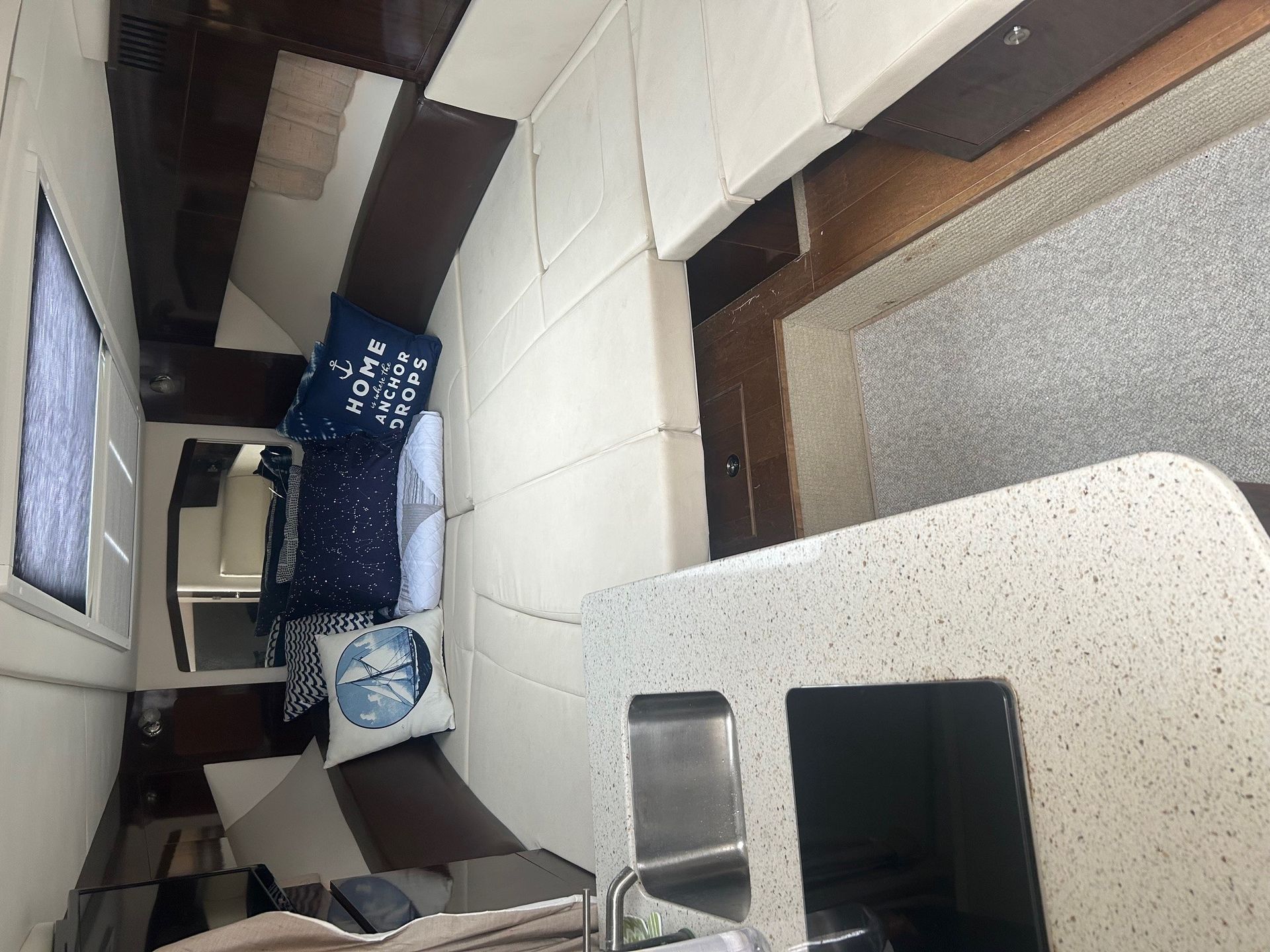 Interior view of a boat kitchen. White countertop, dark brown cabinetry, pillows on a bench, and a window.