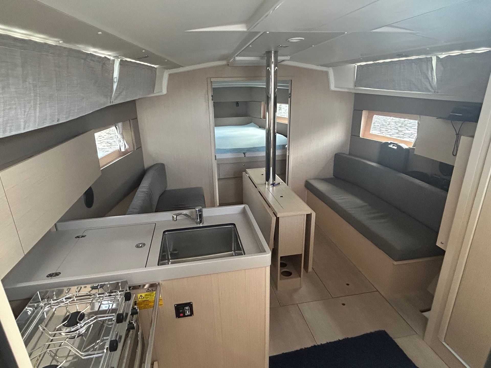 Interior of a sailboat cabin: galley with stove, sink, seating, and a berth in the back.