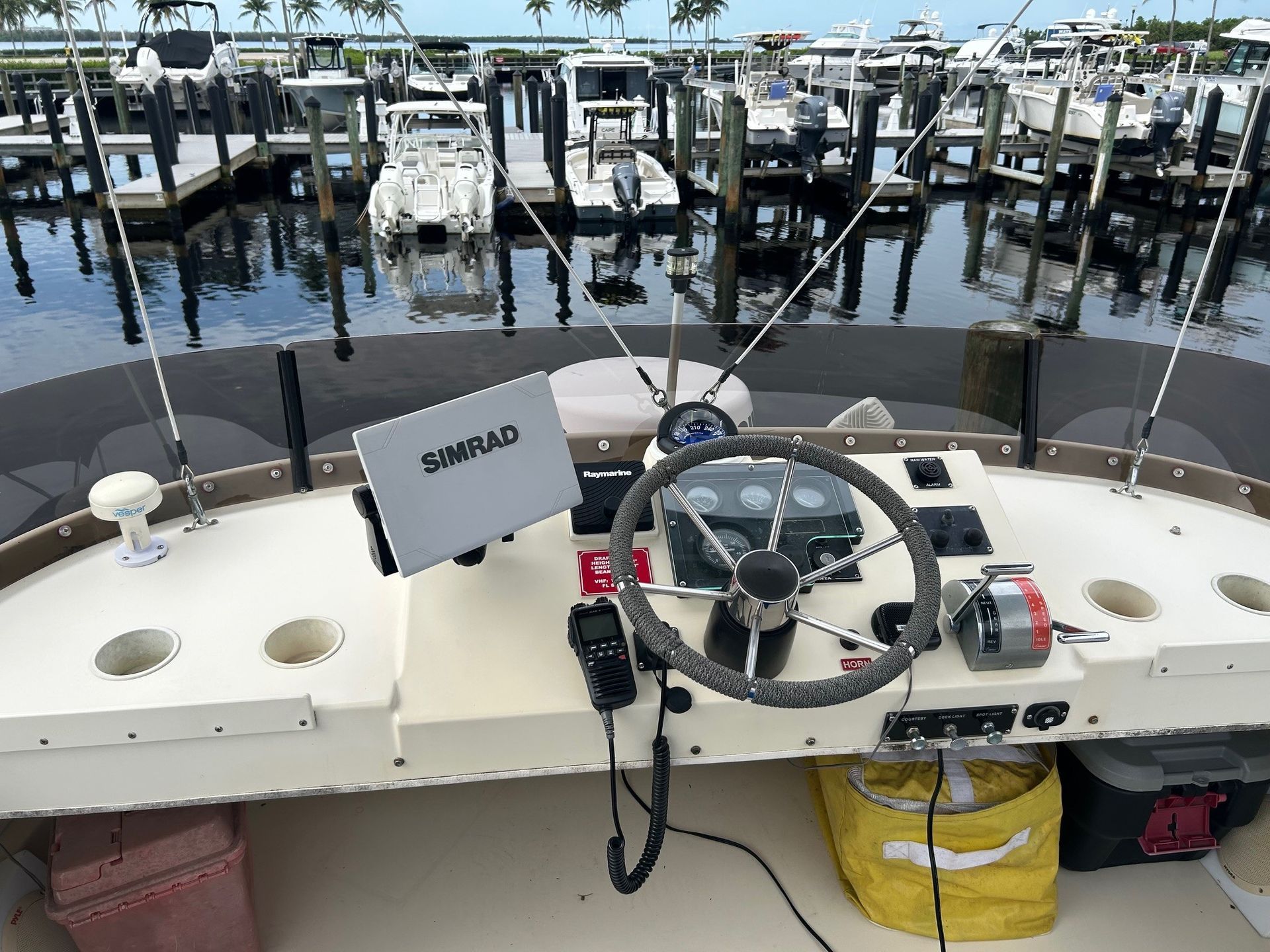 Boat's helm with a steering wheel and navigation equipment, docks in the background.