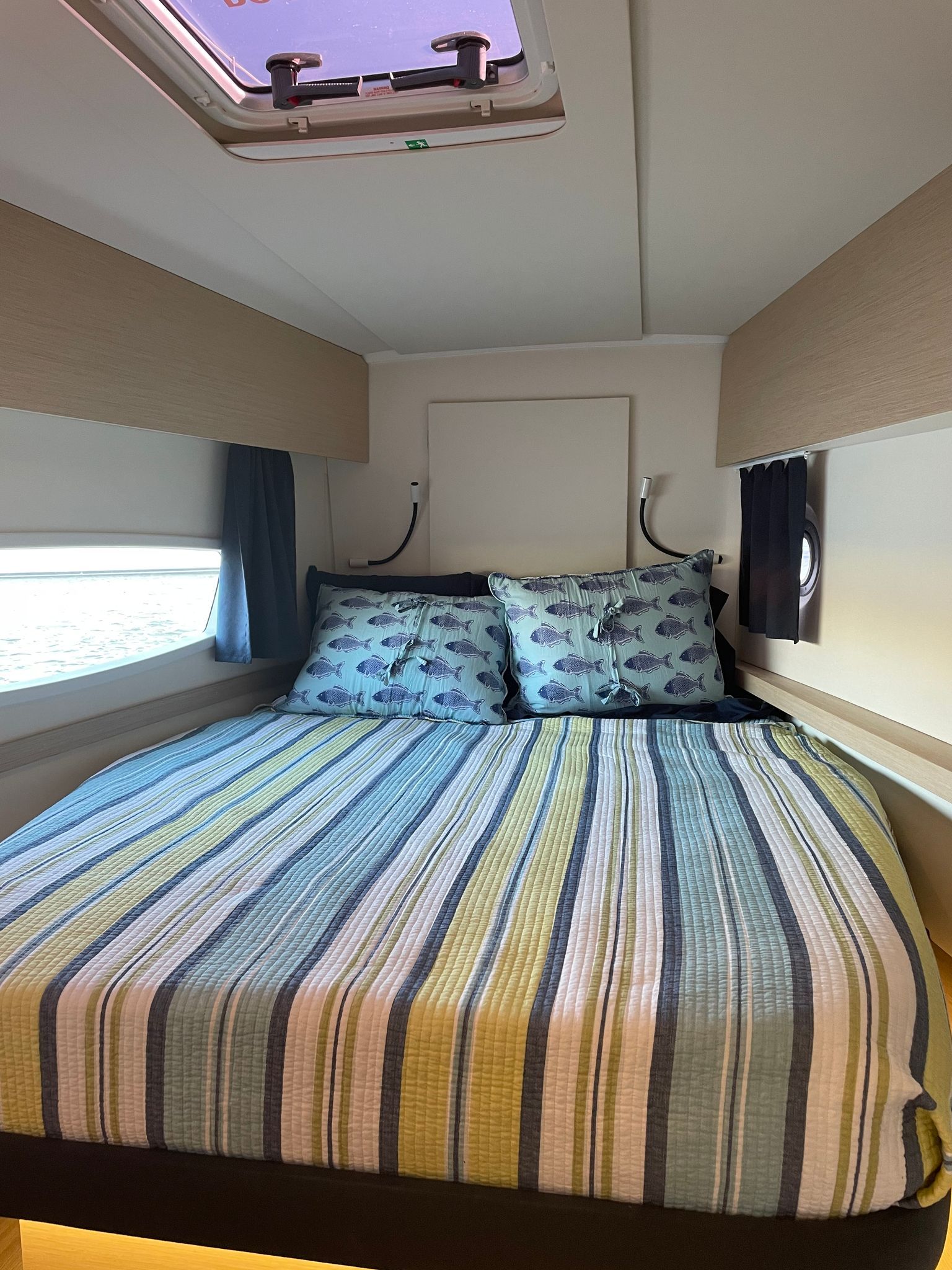 A bed with a striped blanket and pillows in a room with a skylight.
