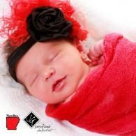 Sleeping baby wrapped in a bright pink blanket, wearing a black and red headband with a flower.
