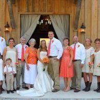 Wedding party posing in front of a wooden church entrance, with bride and groom centered.