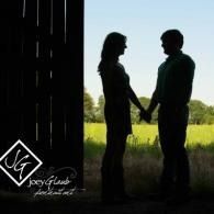 Silhouetted couple holding hands in a doorway, facing each other against a bright grassy field.