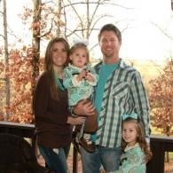Family of four standing on a porch with autumn trees in the background