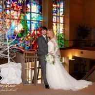 Bride and groom posing in a church beside a colorful stained-glass window
