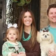 Family posing on a porch with a small white dog, smiling at the camera.