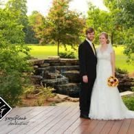 Bride and groom posing outdoors beside a small waterfall and garden pond