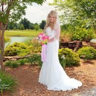 Woman in a white wedding dress holding a pink bouquet in a garden by a pond