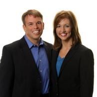 Two smiling professionals standing together in dark business attire against a white background