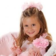 Smiling child in pink dress holding a baby with a pink flower headband, against a soft white background