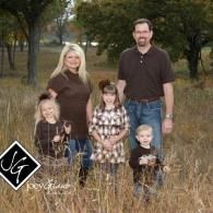 Family of five standing in tall grass outdoors, with trees in the background.