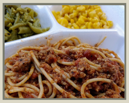 Spaghetti with meat sauce in a divided takeout container, with green beans and corn on the side