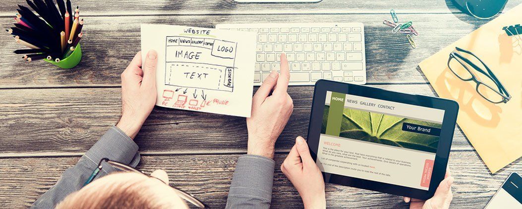 A person is sitting at a wooden table holding a tablet and a piece of paper.