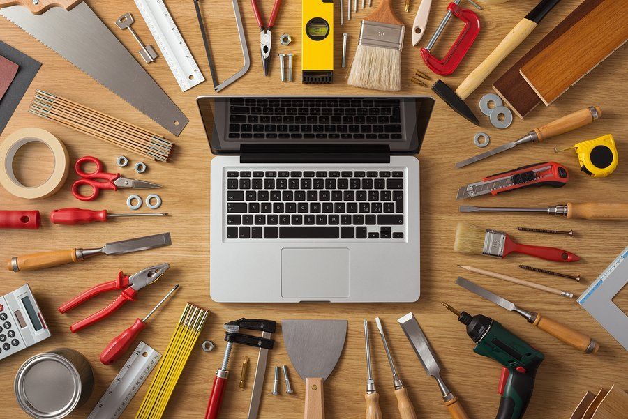 A laptop computer is surrounded by tools on a wooden table.