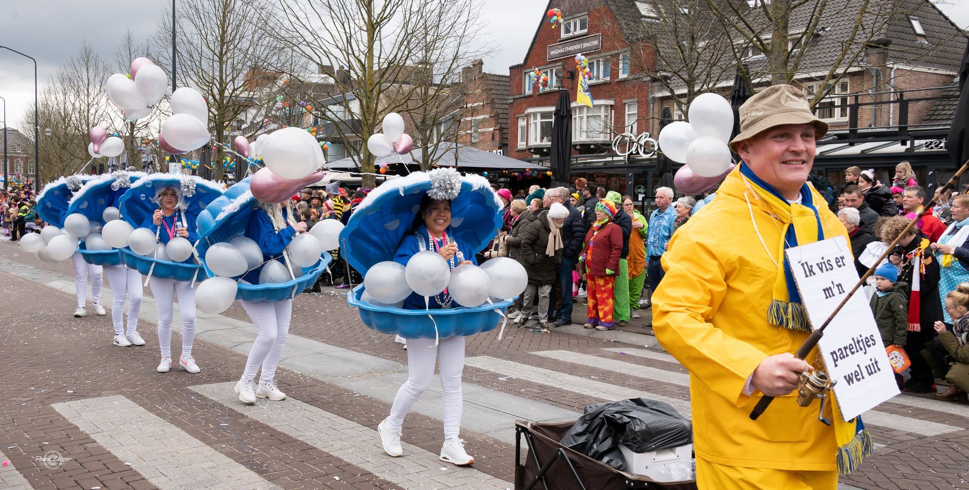 Een man in een gele regenjas houdt een bord vast voor een parade.