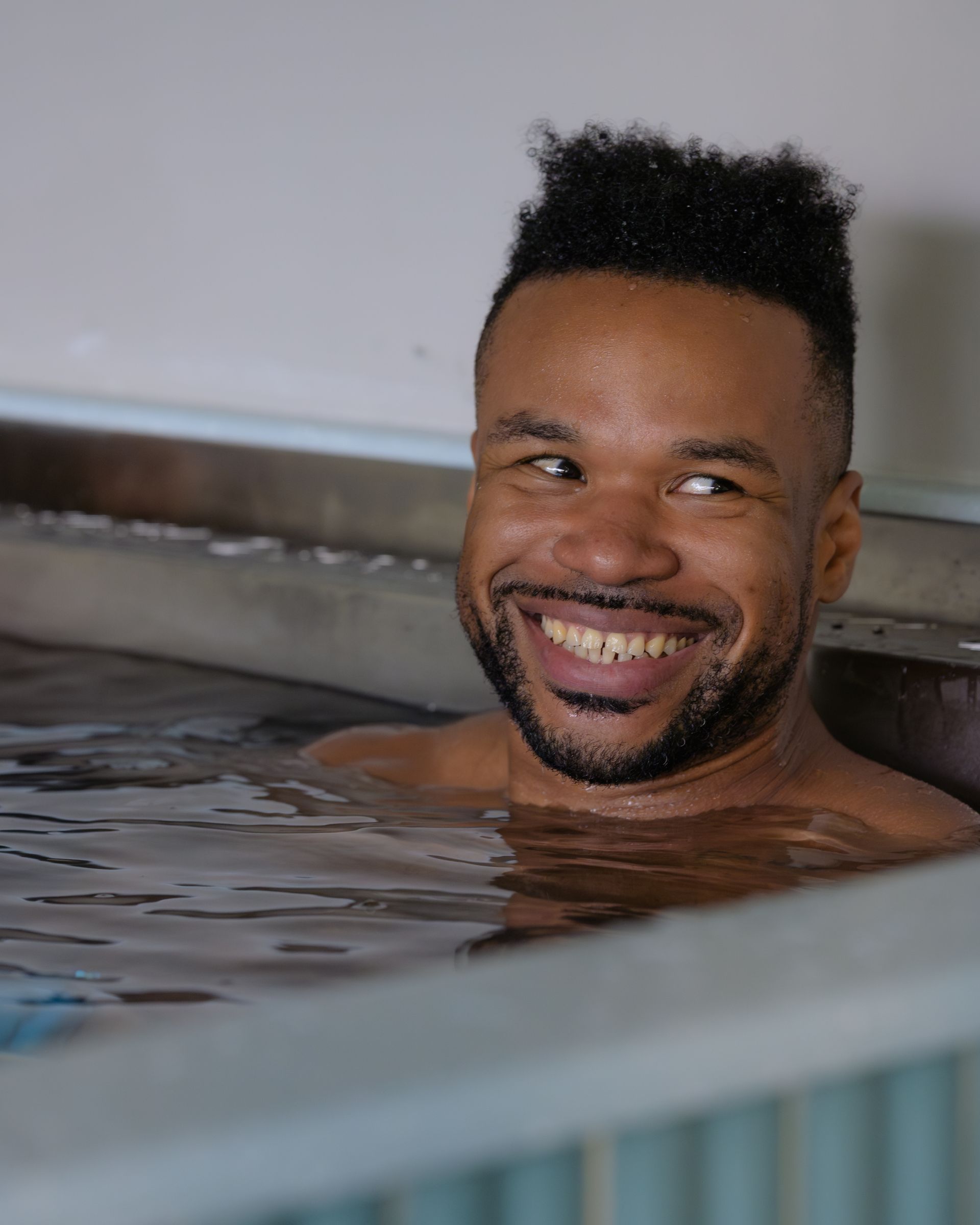 Woman relaxing in a bathtub, eyes closed, arms resting on sides, sunlight on face.