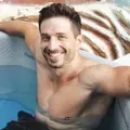 Man with a muscular build in a hot tub, smiling at the camera.