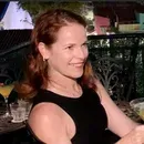 Woman with red hair smiling, wearing a black tank top, outdoors.