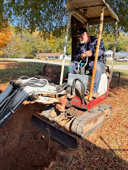 A man is driving a small excavator in a yard.