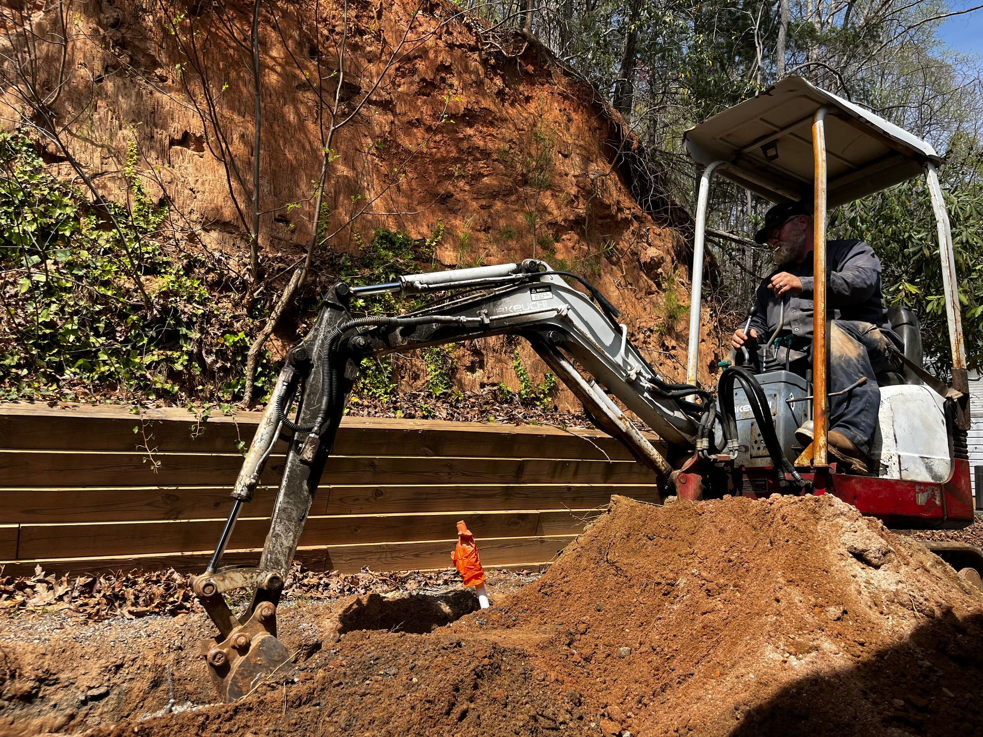 A man is driving a small excavator in a dirt field.