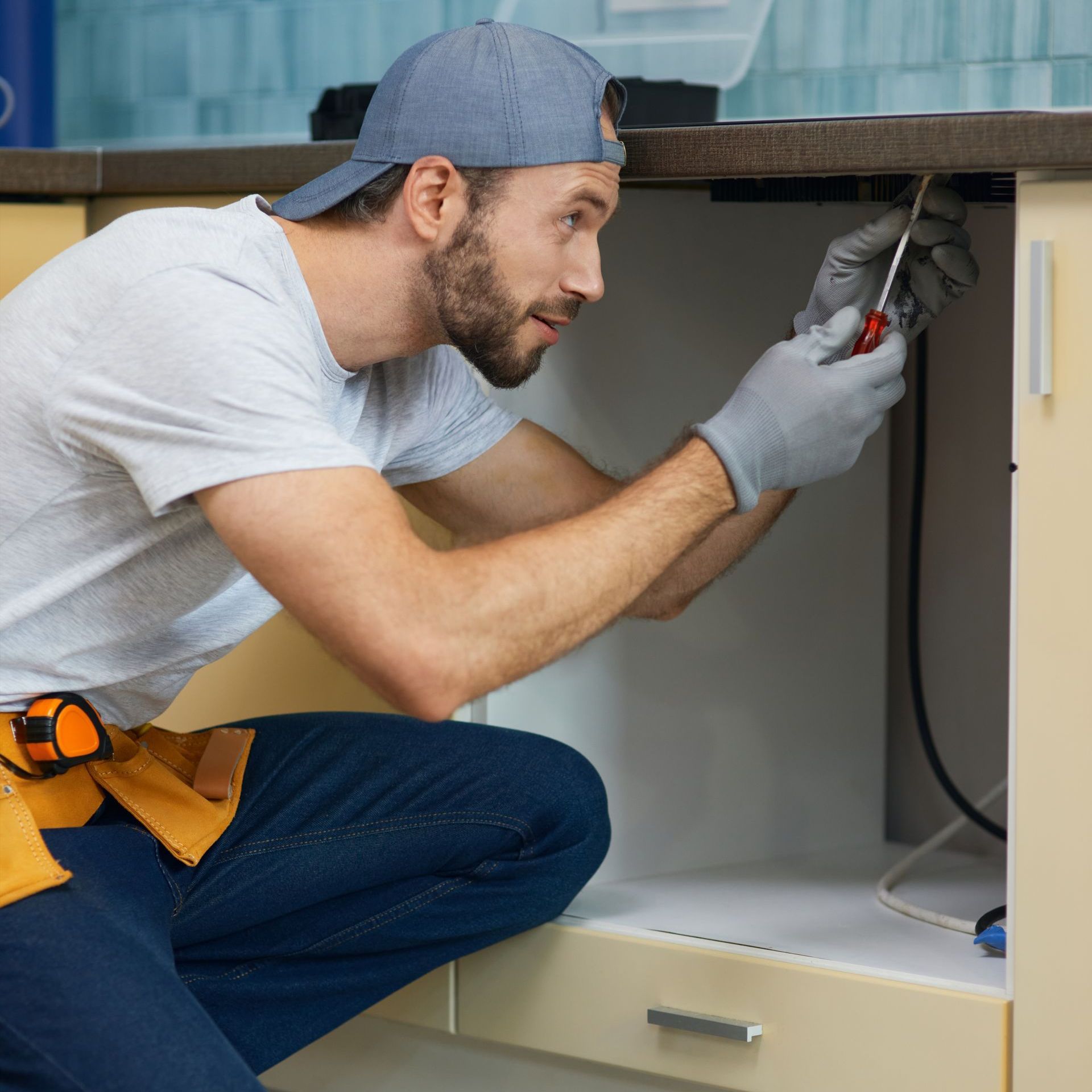 A man is kneeling on the floor fixing a sink in a kitchen.