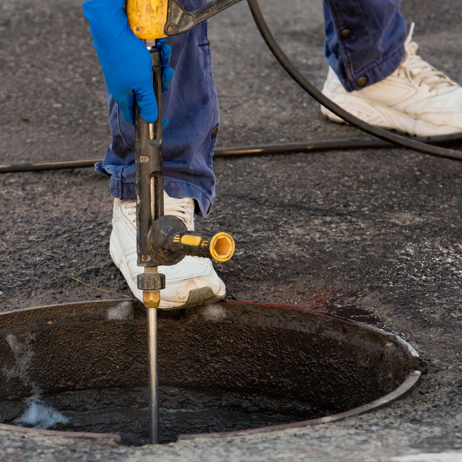 A person is using a drill to drill into a manhole cover