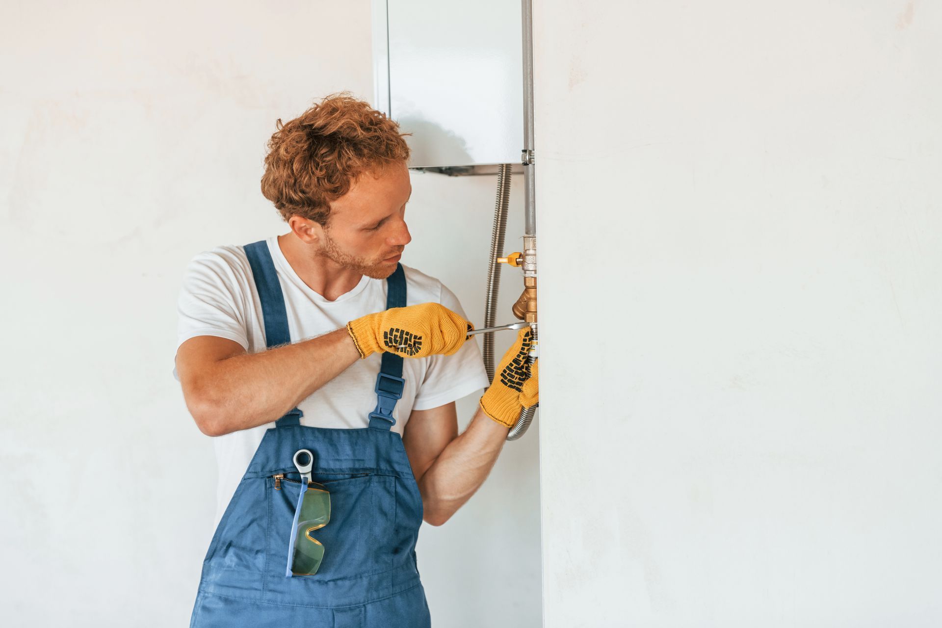 A man in overalls is fixing a boiler on a wall.