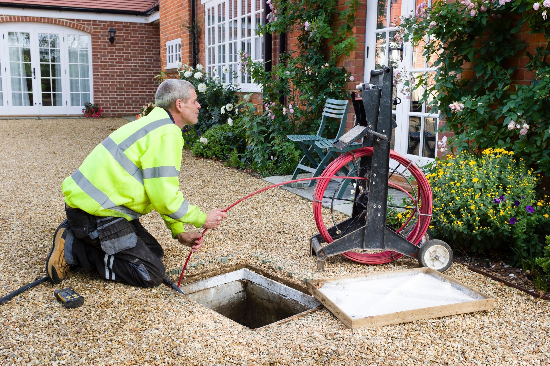 A man is kneeling down in front of a house looking into a drain.