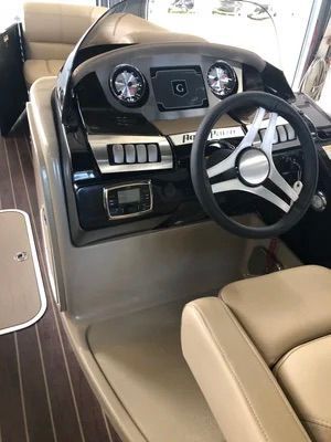 Boat dashboard with gauges, steering wheel, and switches, beige and black, wood flooring.