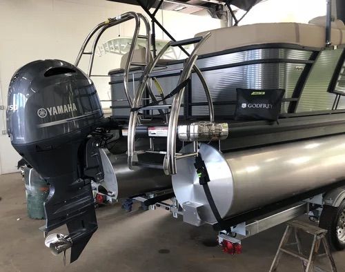 Silver pontoon boat with a Yamaha engine and ladder, parked in a garage.