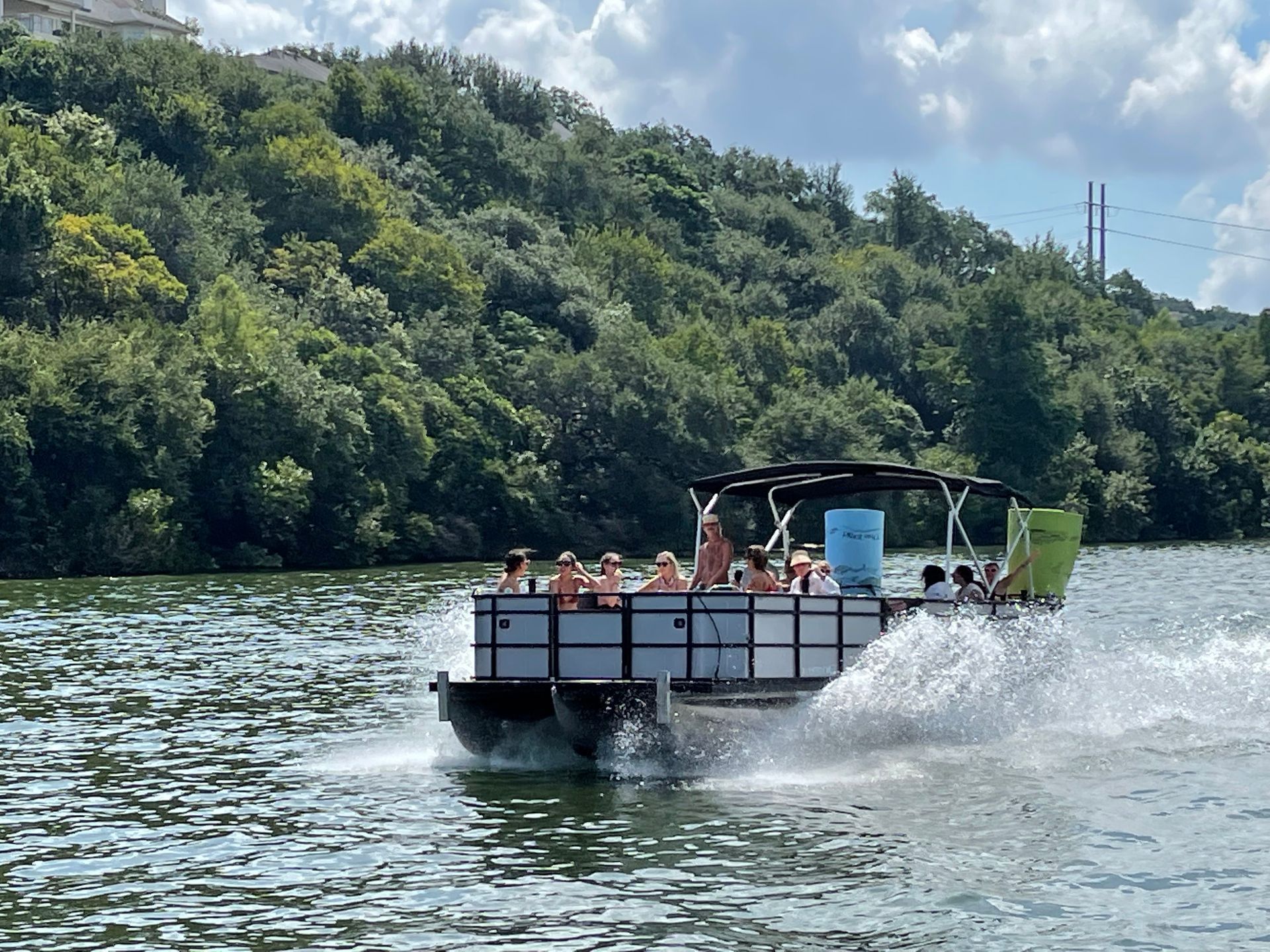 Pontoon boat with people on lake, near wooded hillside.