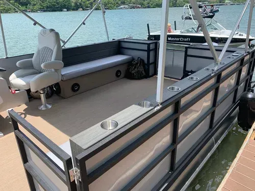 Pontoon boat docked at a pier, featuring seating, cup holders, and a gray and brown deck.