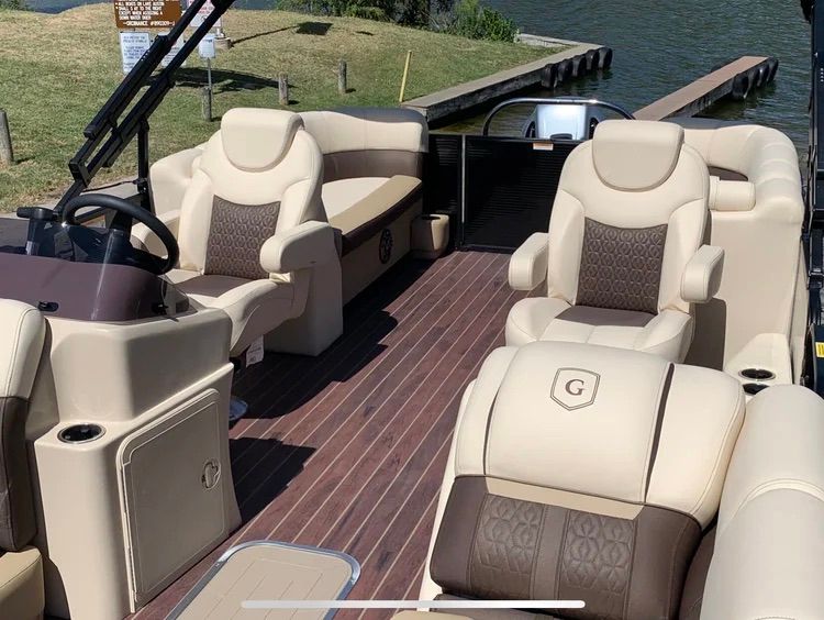 Interior of a luxury pontoon boat with beige and brown seating, wooden deck, and a steering wheel.