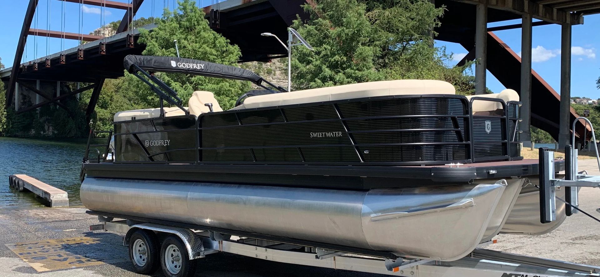 Pontoons on a trailer under a bridge, with trees in the background.