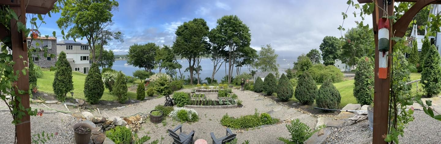 A landscaped garden with a view of the ocean and trees, with a house in the background.