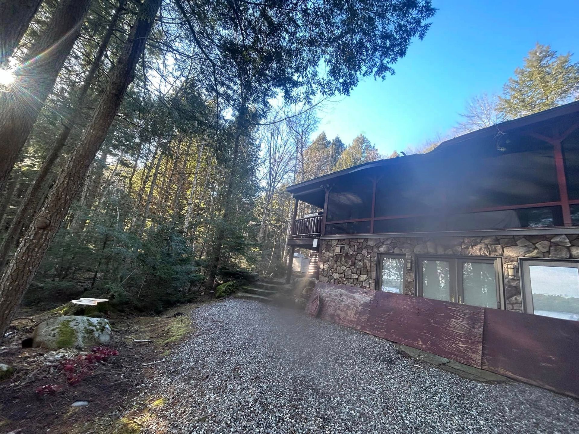 Sunlit cabin nestled among trees, gravel path leads toward the building.