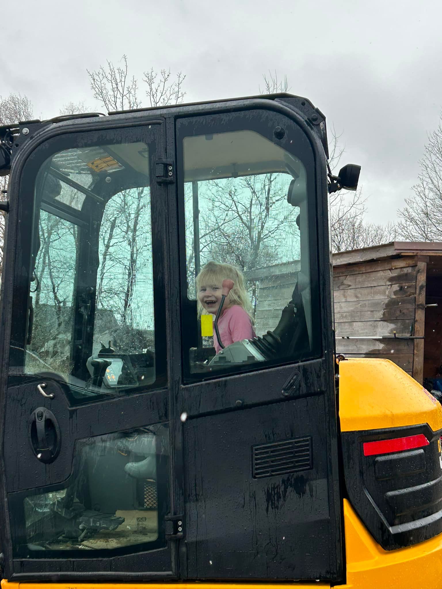 A young girl laughs inside a yellow construction vehicle cab.