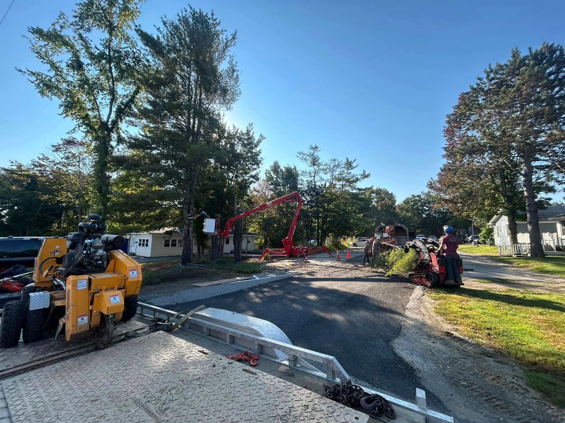 Road construction site with heavy machinery, trees, and blue sky.