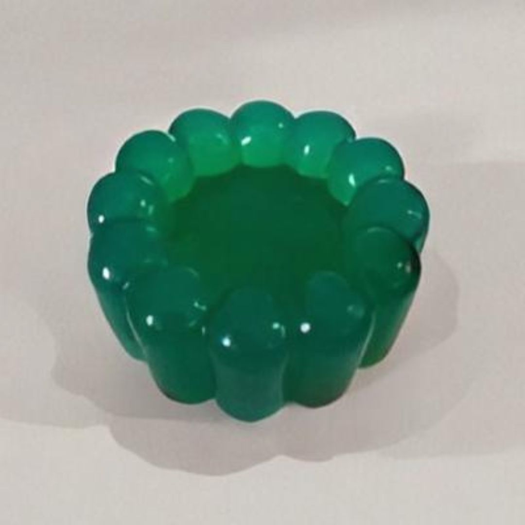 Cenicero verde con forma de flor sobre una superficie blanca. El cenicero es de un verde brillante y translúcido.