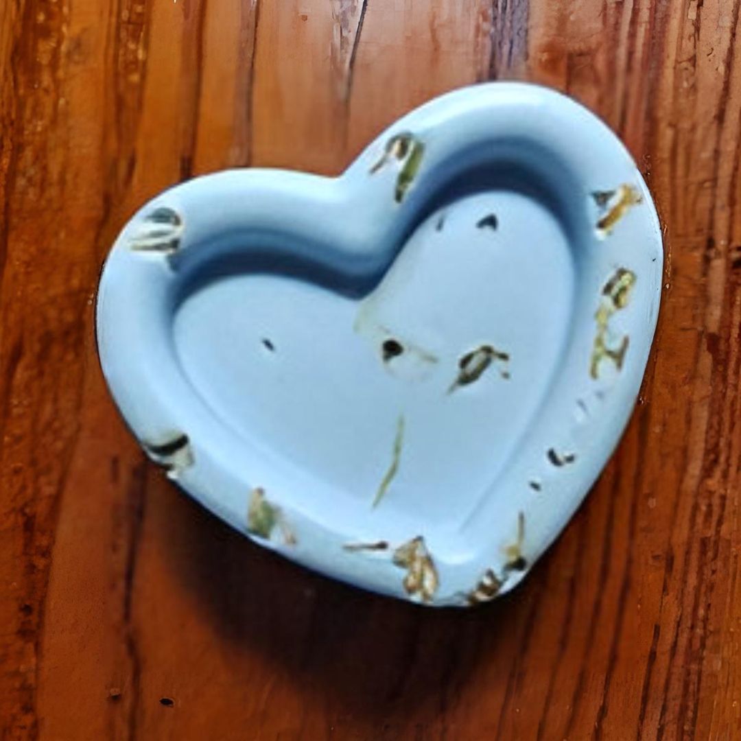 Plato de color azul claro en forma de corazón con hierbas secas incrustadas, apoyado sobre una superficie de madera.