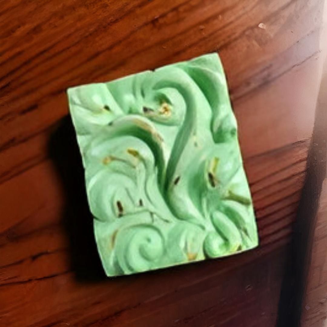 Una barra de jabón verde con diseños decorativos en espiral; reposa sobre una superficie de madera oscura.