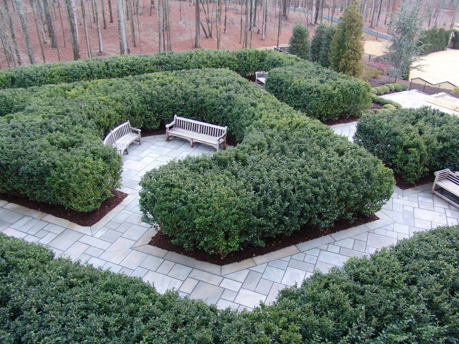 Overhead view of a formal garden with hedges, stone pathways, and benches.