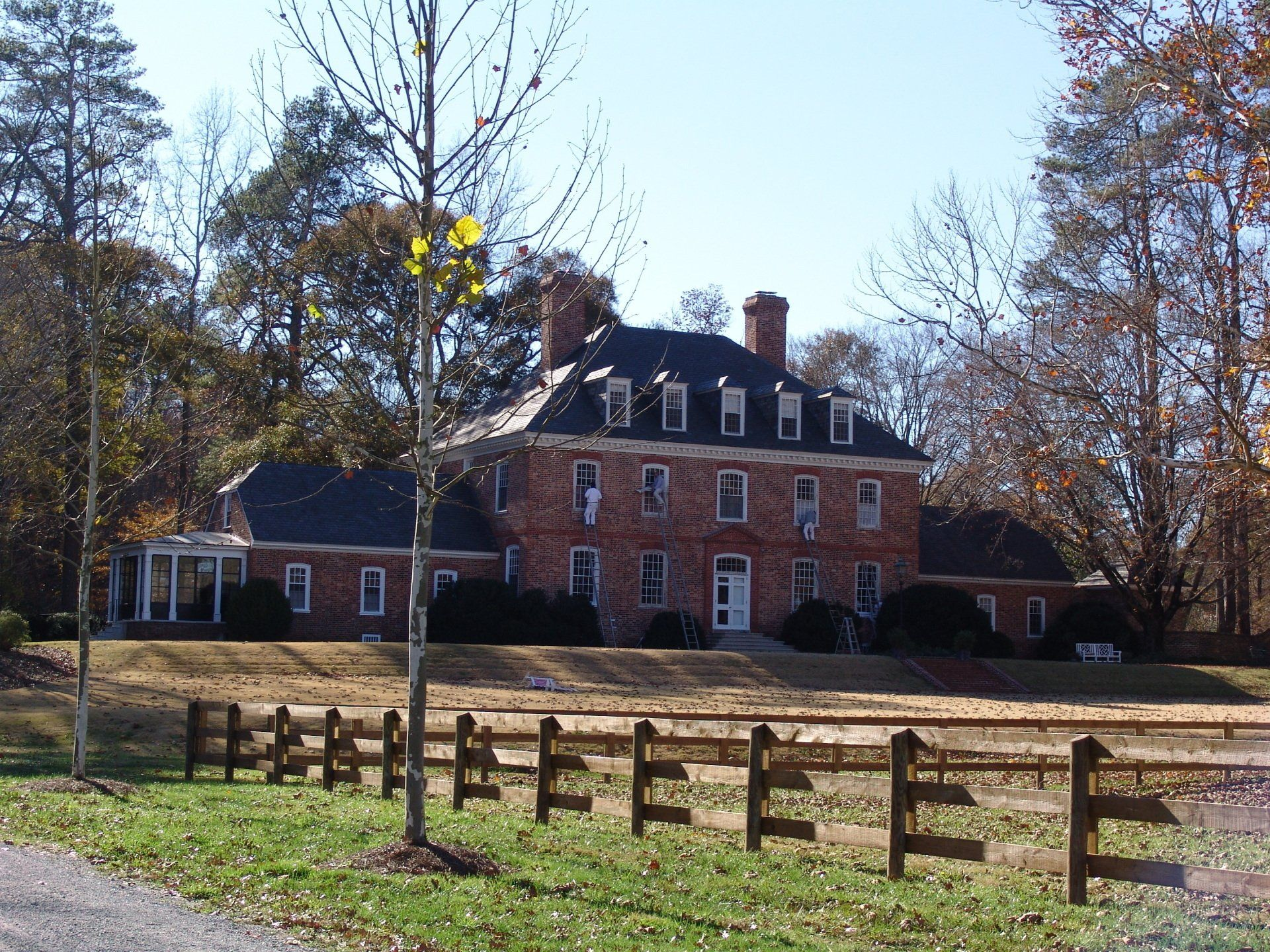 Red brick colonial house with a black roof behind a wooden fence.